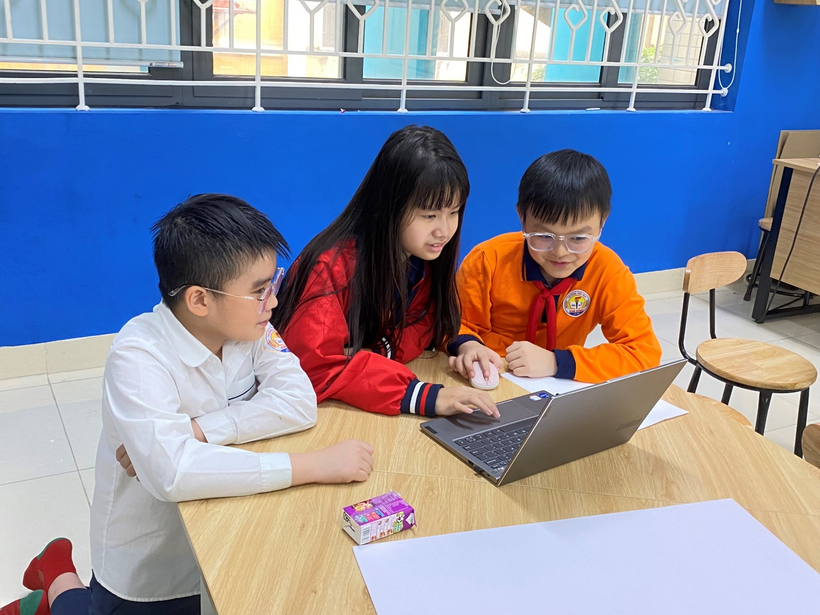 A group of kids sitting at a table looking at a computerDescription automatically generated